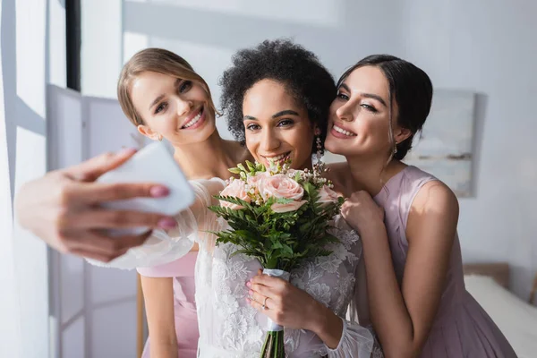 African american bride taking selfie with wedding bouquet and bridesmaids, blurred foreground — Stock Photo