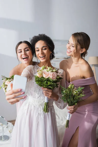 African american bride taking selfie with cheerful bridesmaids at home — Stock Photo