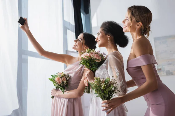 Noiva americana africana com damas de honra segurando buquês de casamento enquanto toma selfie no smartphone — Fotografia de Stock