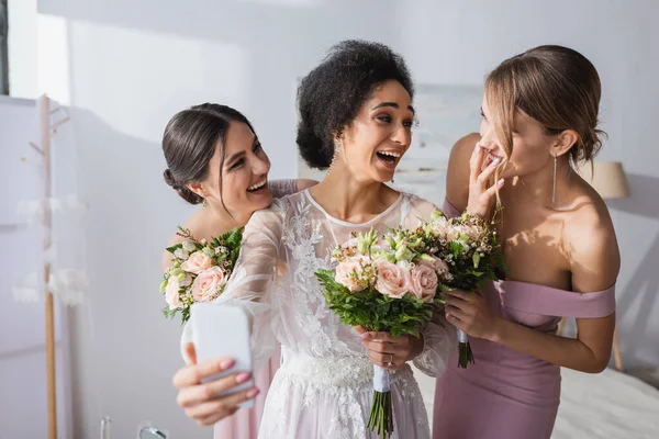 Rire mariée afro-américaine prendre selfie avec des amis gais, flou au premier plan — Photo de stock