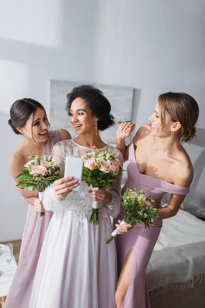 Alegre afroamericana novia tomando selfie con alegre amigos en dormitorio - foto de stock