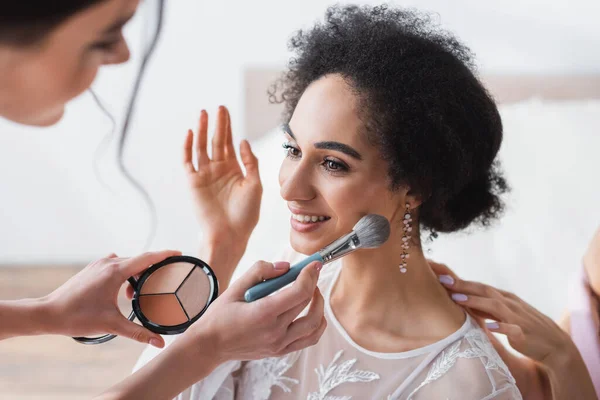 Donna che applica evidenziatore sul viso della sposa afro-americana, primo piano sfocato — Foto stock