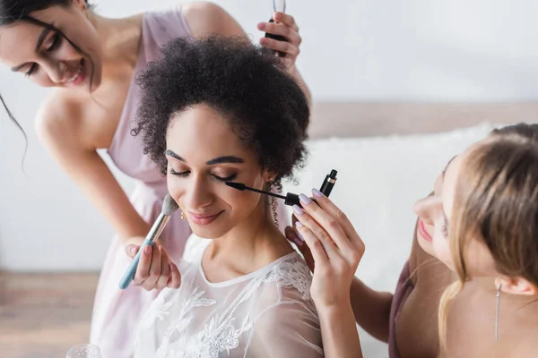 Smiling women doing makeup to pretty african american bride, blurred background — Stock Photo