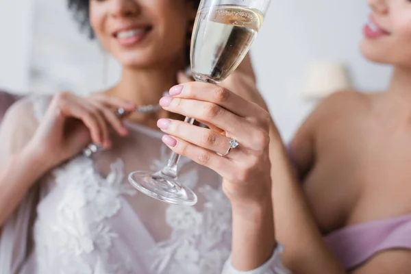 Vista ritagliata della sposa afro-americana in possesso di bicchiere di champagne vicino damigella d'onore su sfondo sfocato — Foto stock