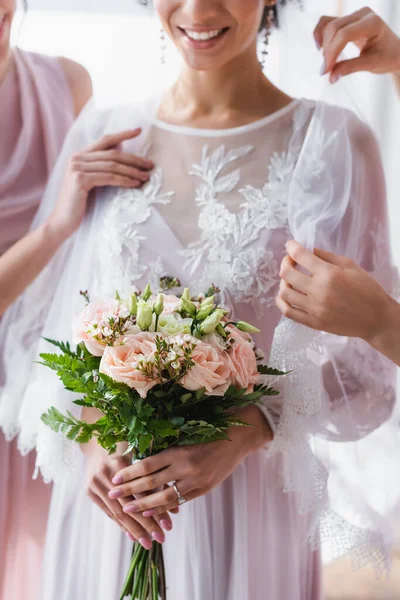 Vista ritagliata della sposa afro-americana con bouquet da sposa vicino alle damigelle d'onore che regolano il velo — Foto stock