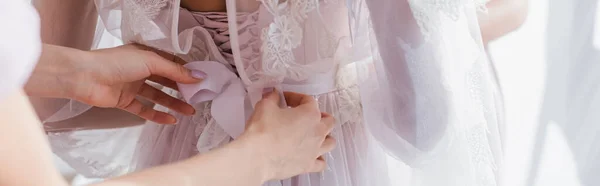Partial view of bridesmaid tying ribbon on dress of bride, blurred foreground, banner — Stock Photo