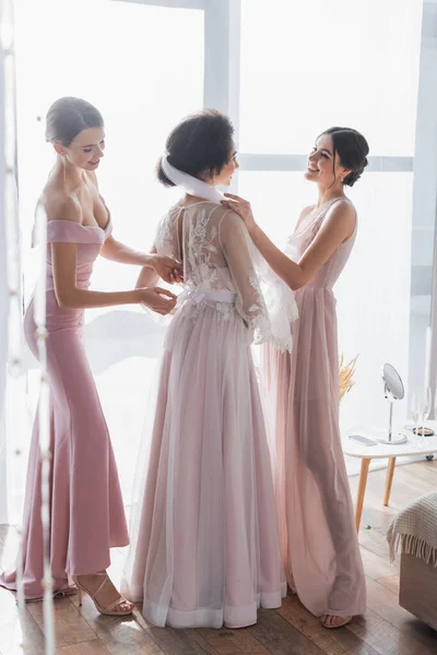 Vista completa de damas de honor multiculturales preparando mujer afroamericana para la boda - foto de stock