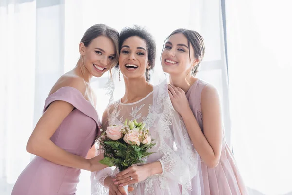 Feliz africana americana novia sonriendo a cámara cerca alegre damas de honor - foto de stock