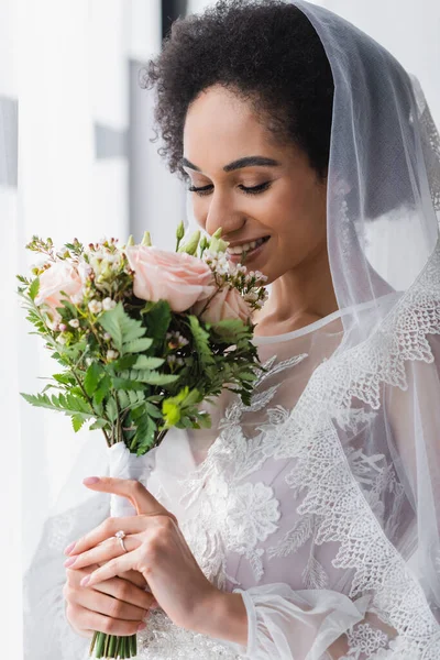 Sorridente noiva afro-americana desfrutando cheiro de buquê de casamento — Fotografia de Stock