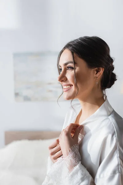 Sposa gioiosa in abito di raso guardando lontano in camera da letto — Foto stock