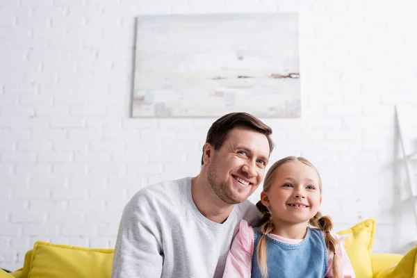 Alegre padre e hija mirando hacia otro lado y sonriendo en casa - foto de stock