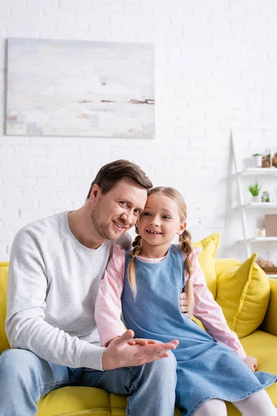 Glückliches Kind, das die Hand des Vaters berührt, der sie zu Hause auf dem Sofa umarmt — Stockfoto