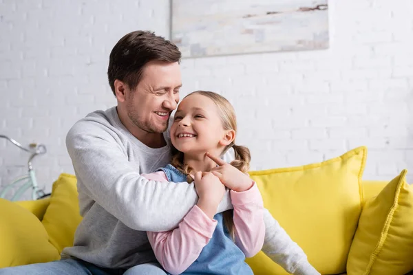 Overjoyed man with daughter hugging on sofa at home — Stock Photo