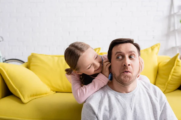 Joyeuse fille bouchant les oreilles de père grimaçant tout en s'amusant à la maison — Photo de stock