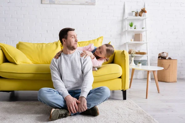 Uomo seduto sul pavimento e smorfie vicino figlia felice — Foto stock