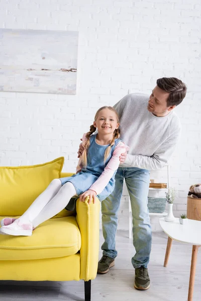 Man touching shoulders of cheerful child sitting on sofa in living room — Stock Photo