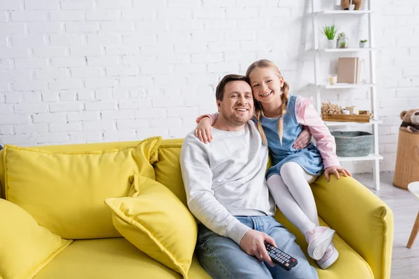 Счастливые отец и дочь смотрят телевизор на диване дома — стоковое фото