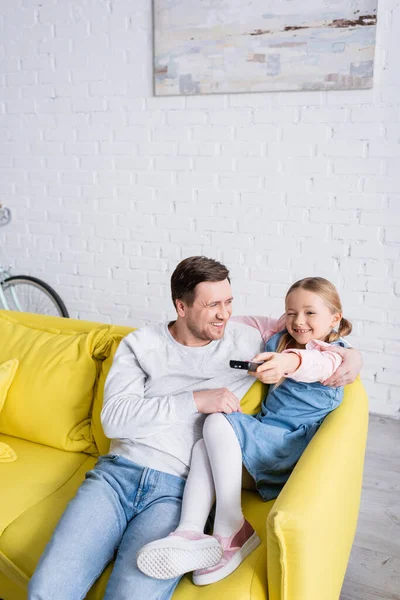 Fröhliches Kind klickt Kanäle auf Fernbedienung, während es mit Vater fernsieht — Stockfoto