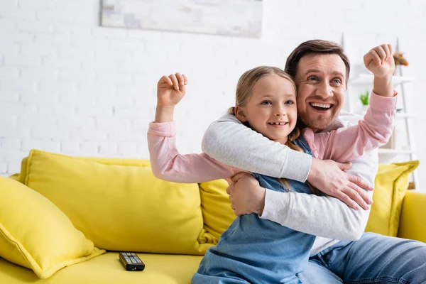 Счастливый отец обнимает дочь показывая победный жест во время просмотра телевизора — стоковое фото