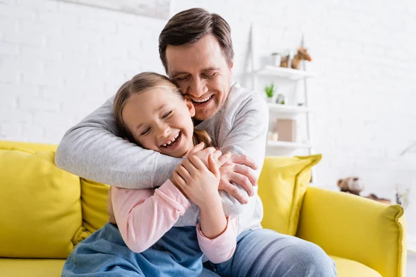 Смеющийся мужчина обнимает дочь на диване в гостиной — стоковое фото