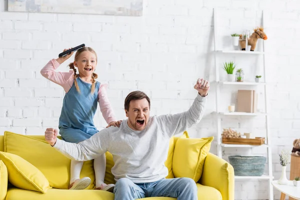 Hombre emocionado gritando y mostrando el gesto de ganar mientras ve la televisión con su hija - foto de stock