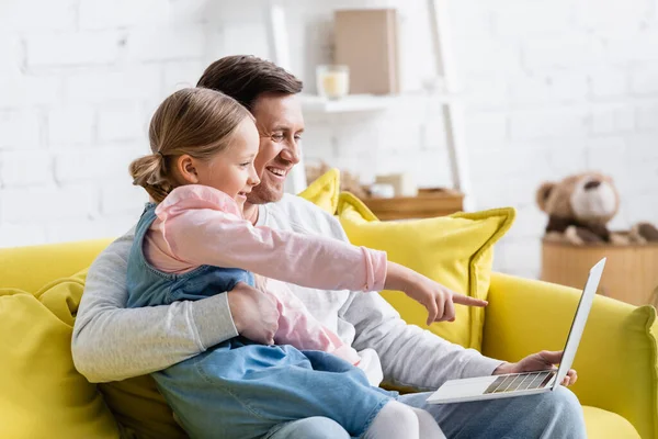 Uomo allegro abbracciando figlia che punta al computer portatile mentre guarda il film — Foto stock