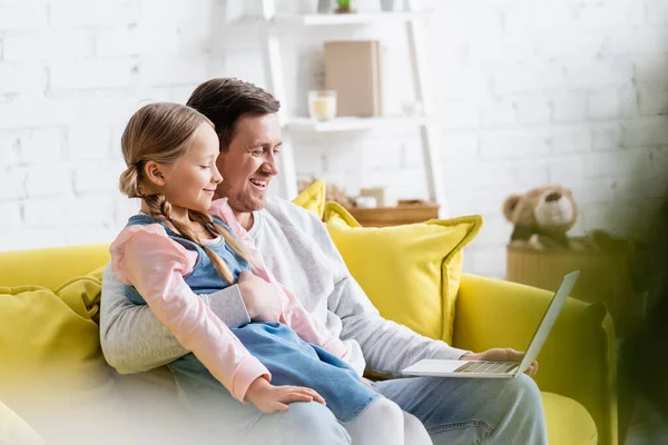 Cheerful man hugging daughter while watching movie on laptop on couch — Stock Photo