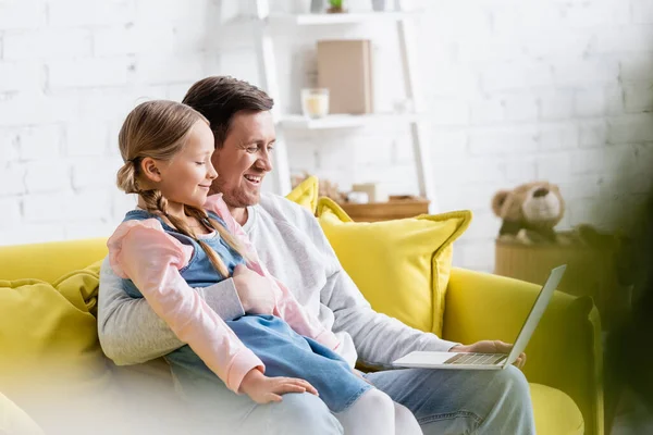 Allegro uomo abbracciando figlia mentre guarda film sul computer portatile sul divano — Foto stock