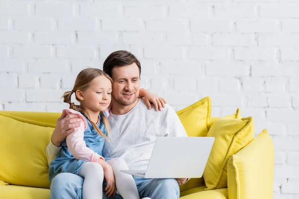 Мужчина обнимает дочь во время просмотра фильма на ноутбуке дома — стоковое фото