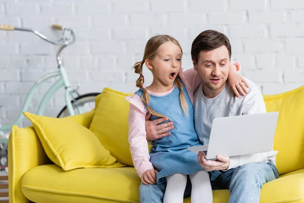 Niño asombrado viendo la película en el ordenador portátil con el padre en casa - foto de stock