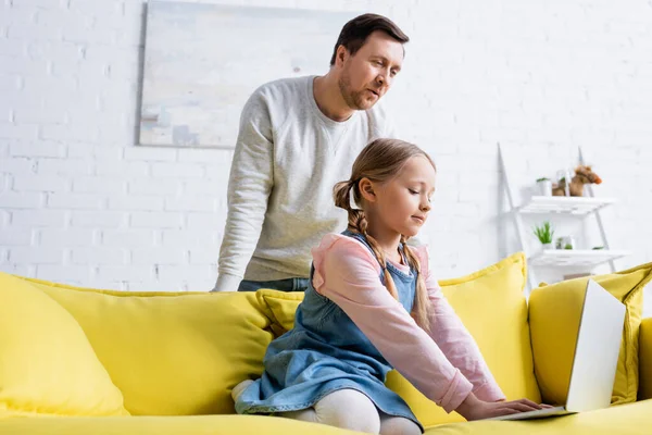 Uomo sorpreso guardando la figlia che digita sul computer portatile sul divano — Foto stock