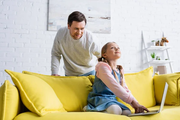 Smiling man near thoughtful daughter typing on laptop at home — Stock Photo