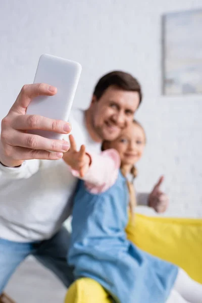 Smiling man taking selfie with daughter and showing like on blurred background — Stock Photo