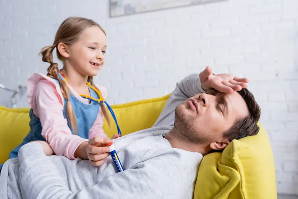 Homme prétendant malade près de fille souriante mesurant sa température avec un thermomètre jouet — Photo de stock