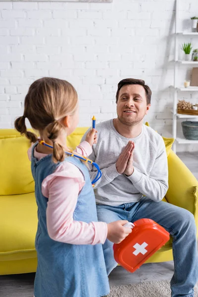 Father showing please gesture near daughter holding toy syringe and first aid kit — Stock Photo