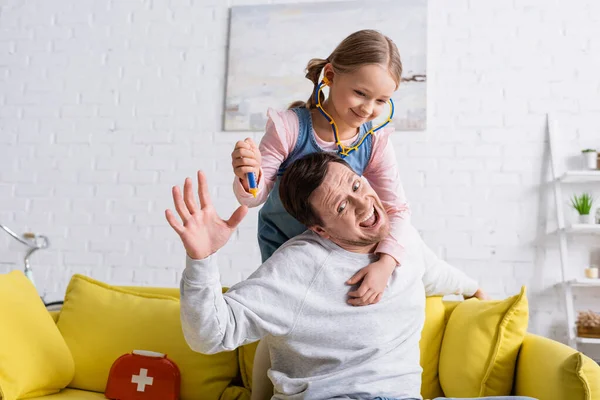 Homem gritando enquanto finge assustado perto filha segurando brinquedo seringa — Fotografia de Stock