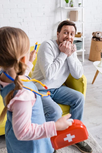 Homme feignant effrayé près de fille tenant seringue jouet sur le premier plan flou — Photo de stock