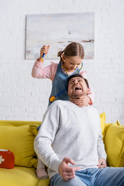 Мужчина кричит, притворяясь испуганным рядом с дочерью, держащей игрушечный шприц — стоковое фото