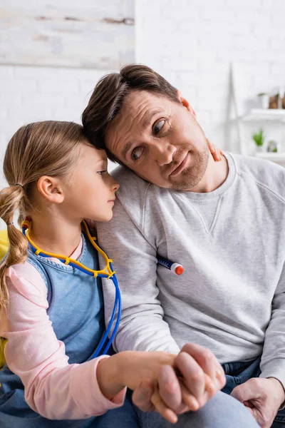 Kind umarmt Vater und misst Temperatur mit Spielzeugthermometer — Stockfoto