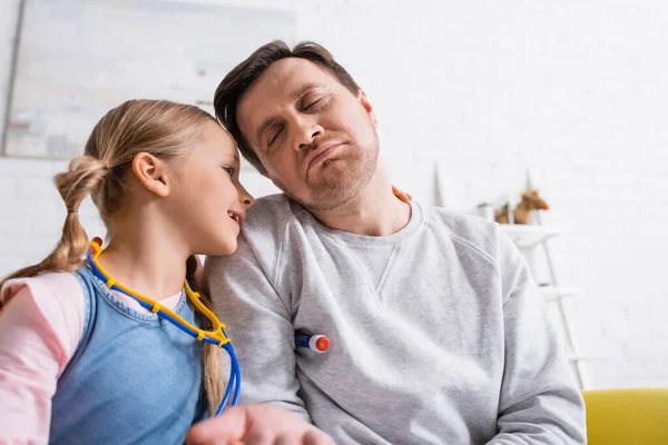 Ragazza con giocattolo stetoscopio giocare medico vicino padre fingendo malato — Foto stock