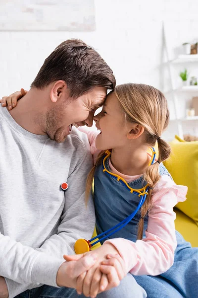 Padre e hija emocionados tomados de la mano mientras juegan médico y paciente en casa - foto de stock