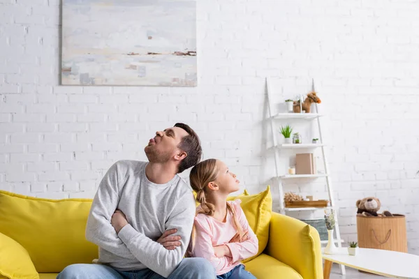 Ofendido hombre con hija sentado con los brazos cruzados y sacando lenguas - foto de stock