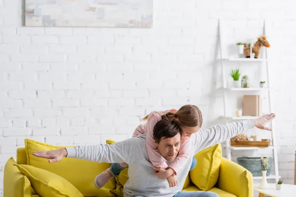 Father showing flight gesture while piggybacking daughter at home — Stock Photo