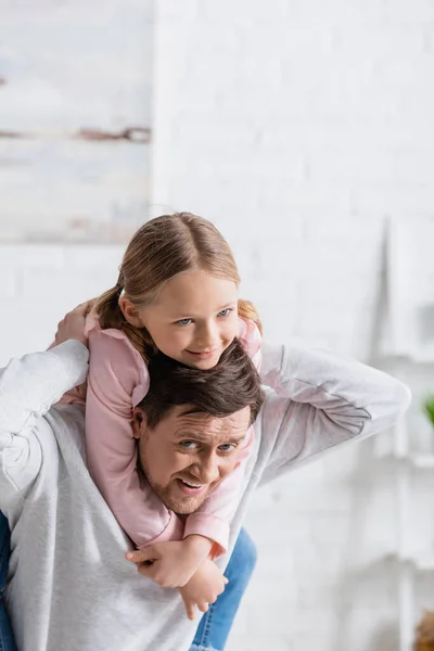 Happy man looking at camera while piggybacking daughter at home — Stock Photo