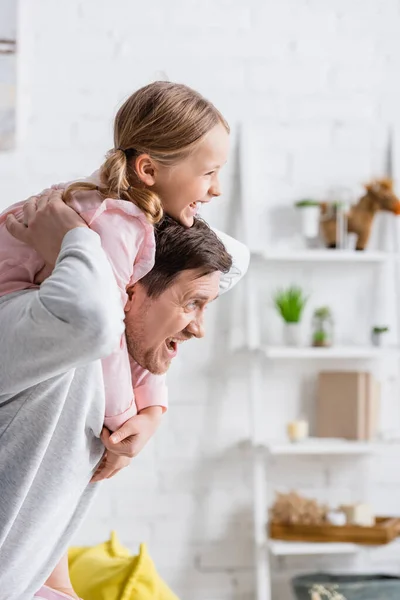 Cheerful man piggybacking amazed daughter while having fun at home — Stock Photo