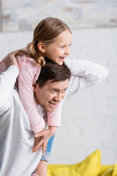 Fröhlicher Mann schaut weg, während Kind huckepack zu Hause ist — Stockfoto