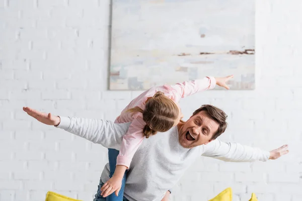 Excited man showing fly gesture while piggybacking daughter at home — Stock Photo