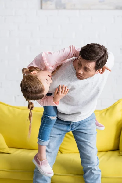 Uomo allegro sporgere la lingua mentre si diverte con la figlia a casa — Foto stock