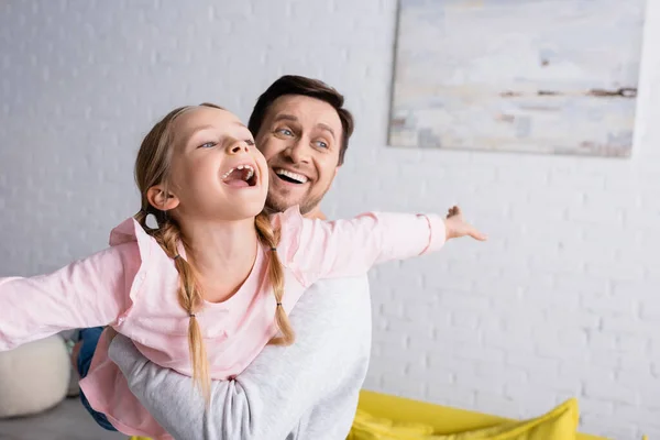 Feliz hombre sosteniendo sorprendido hija mostrando gesto de mosca mientras se divierten en casa - foto de stock