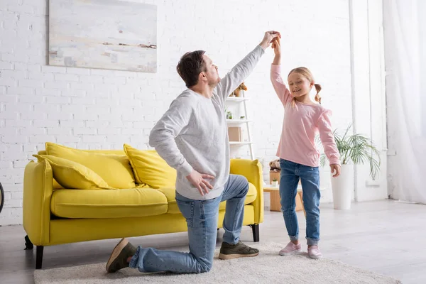 Happy girl having fun while dancing with father standing on knee at home — Stock Photo